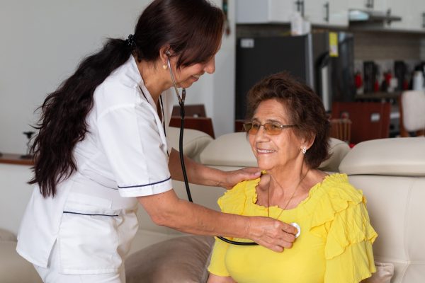 Nurse examining an elderly woman with a stethoscope at a home health checkup. Checking the health status of an elderly patient.